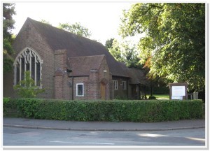 Trinity Methodist Church A small brick church with a steep roof, surrounded by trees and a hedge, on a sunny day.